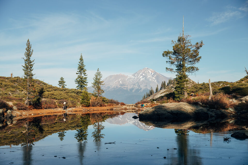 A reflective pond is seen in the foreground with a mountain peak in the distance..