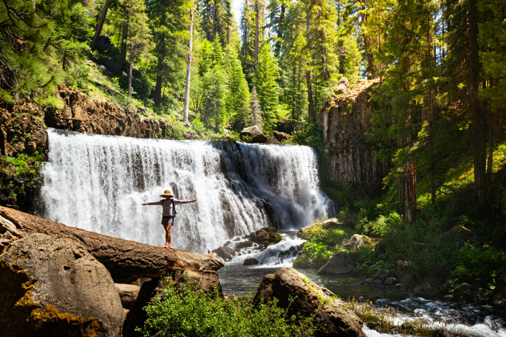 Why your next affordable vacation destination should be in this rural Northern California county A woman walks on a log laid out in front of a waterfall.