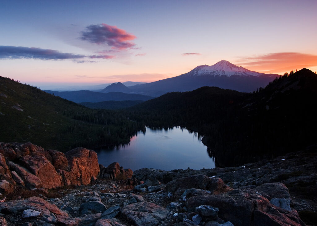 Image depicts a sunrise image of a mountain top in front of a reflective lake