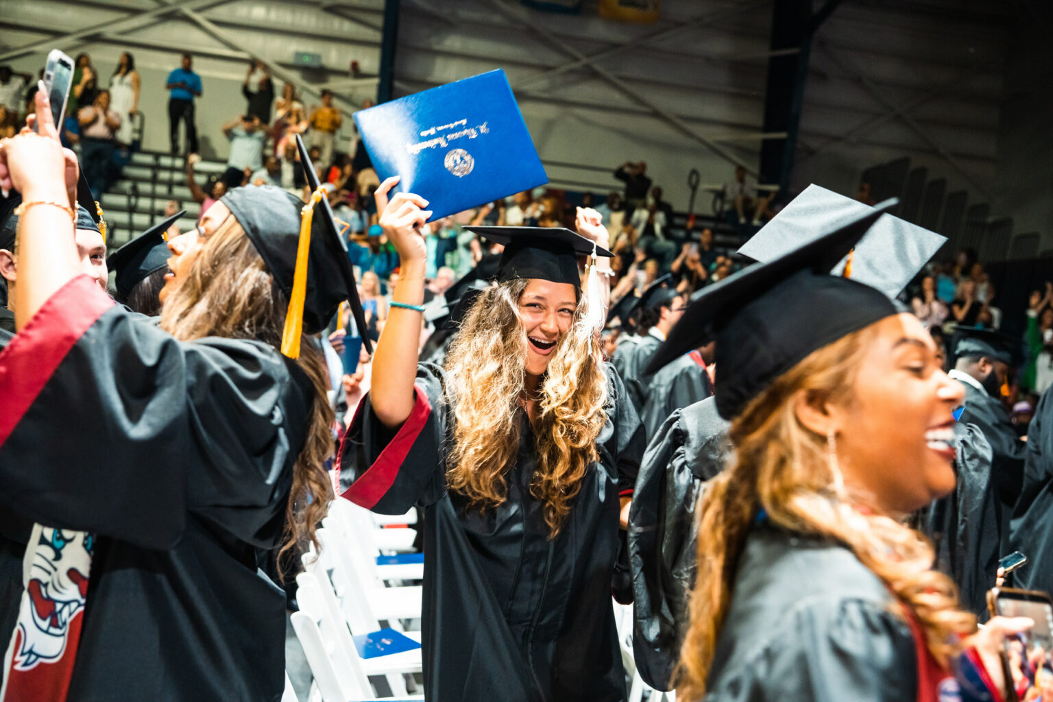A recent college university graduate holds up her degree amongst a crowd of other graduates at St. Thomas University
