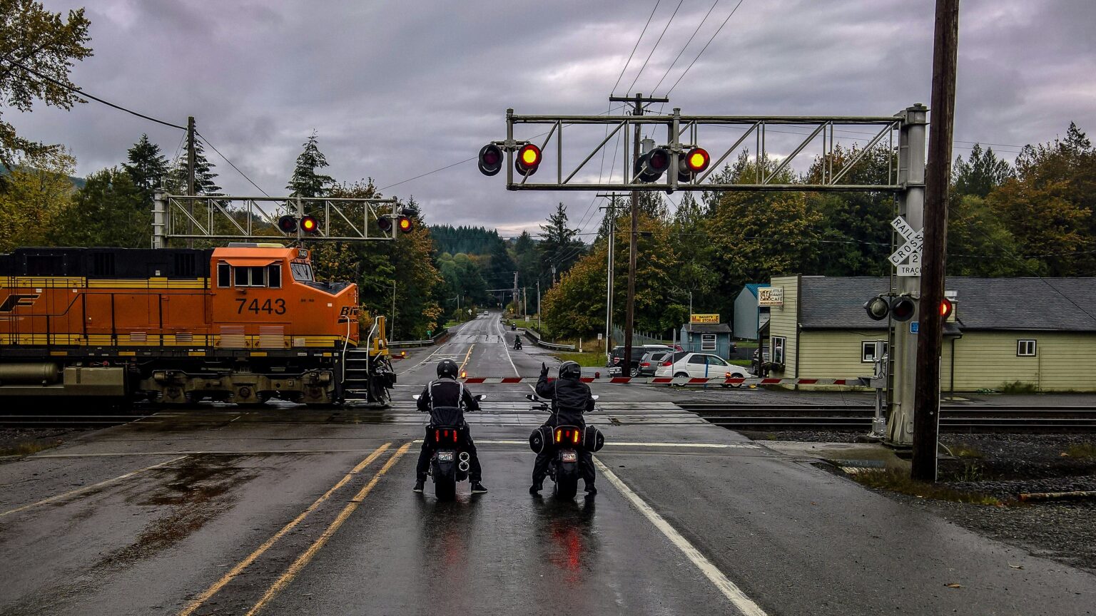 Two motorcyclists wait for a train to cross a railroad crossing.