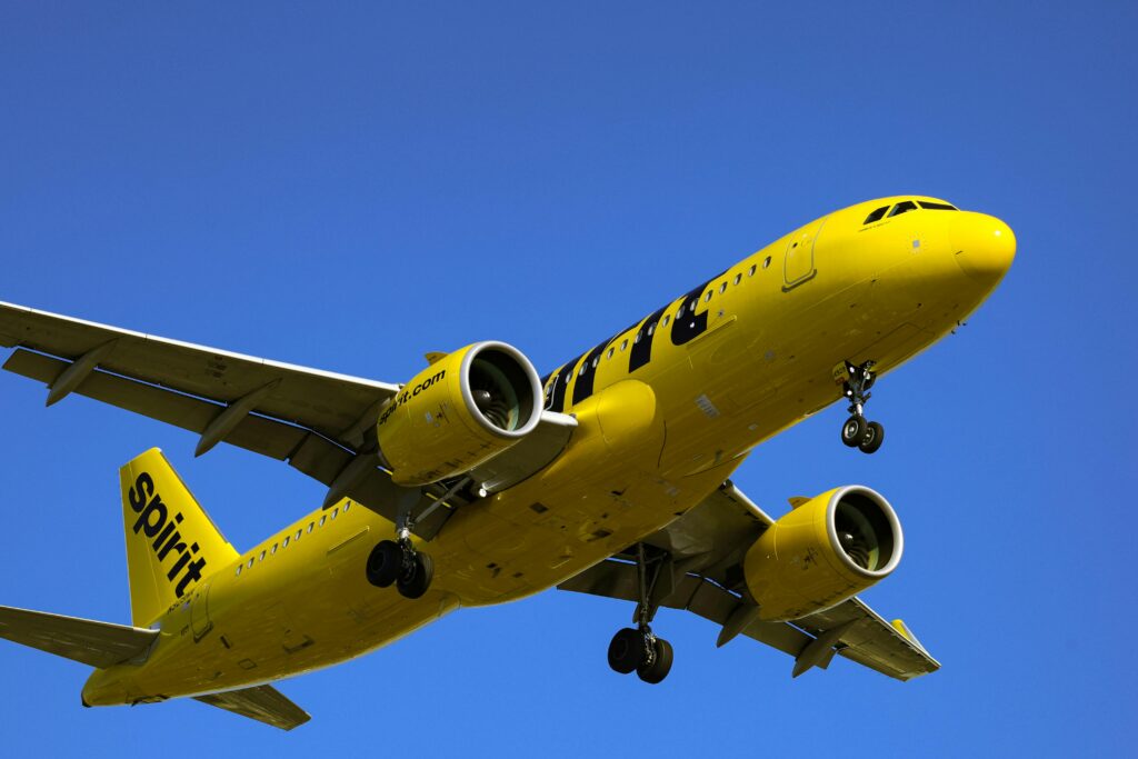 A Spirit Airlines plane flies overhead below a cloudless blue sky. Spirit used to have a hub in Fort Lauderdale