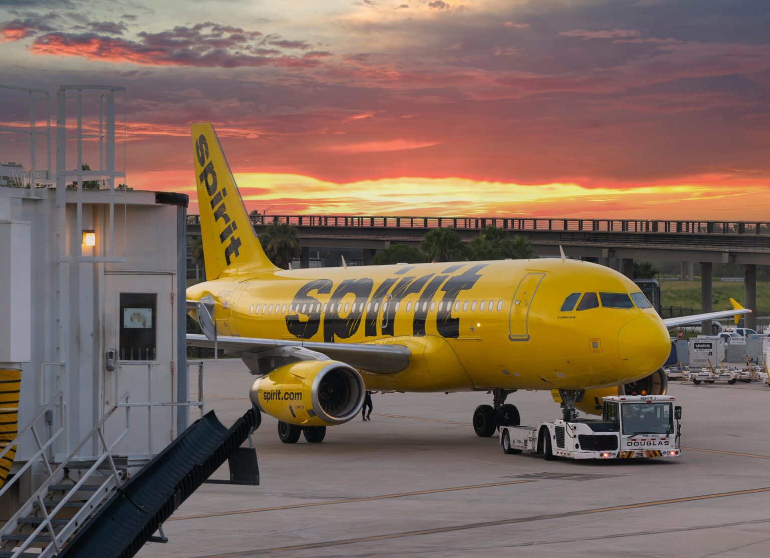 A yellow Spirit Airlines plane sits on a tarmac below a setting sky