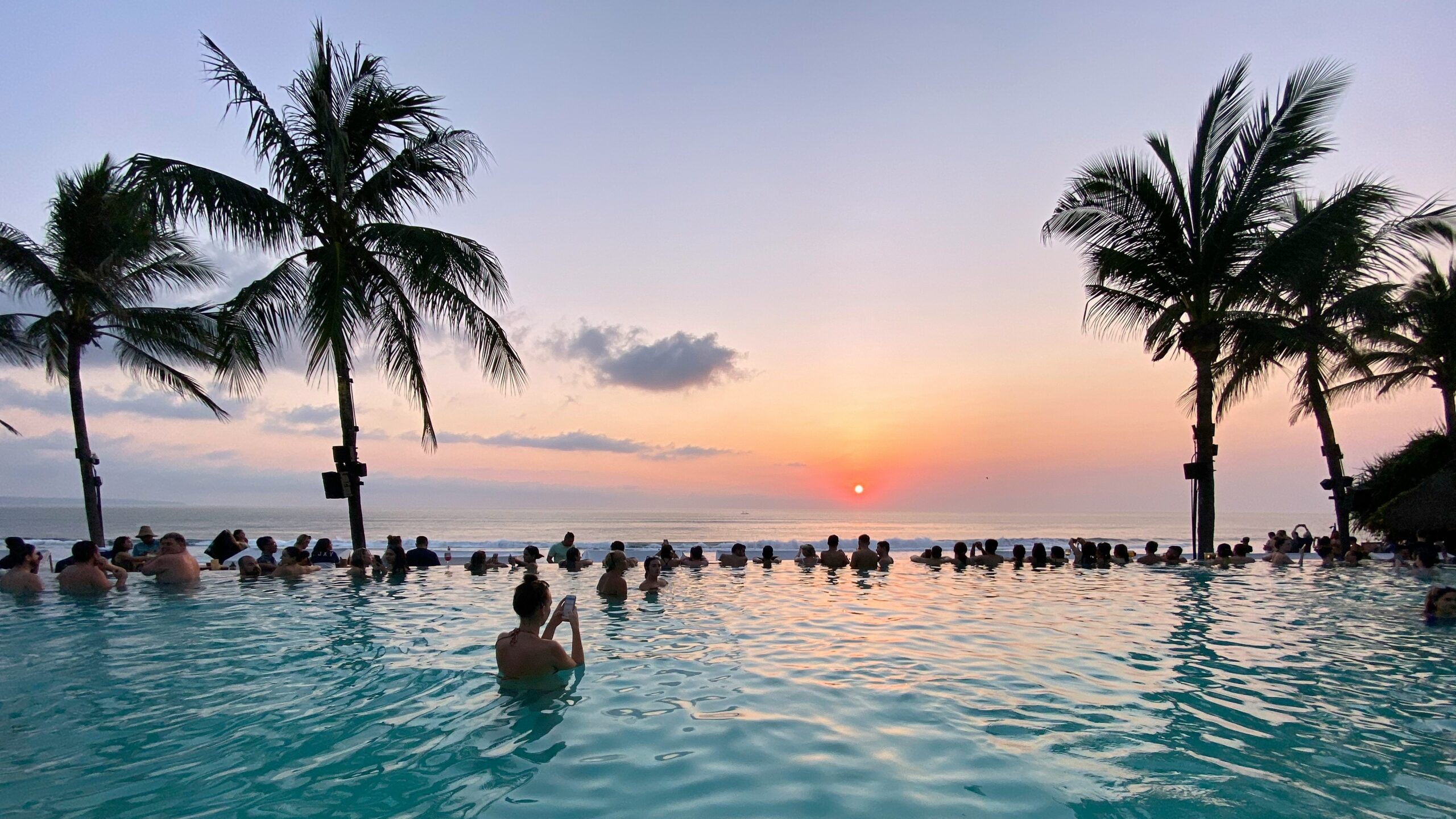 Resortgoers take photos of the setting sun at pool of Potato Head Beach Club in Bali, Indonesia, in this 2019 photo from Unsplash.com