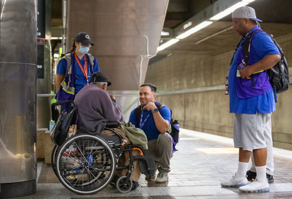 LA Metro says homelessness is down 57% since 2024—will it last? Members of LA Metro's Care-Based Services Division speak with a rider on a train platform in this undated image from The Source blog.