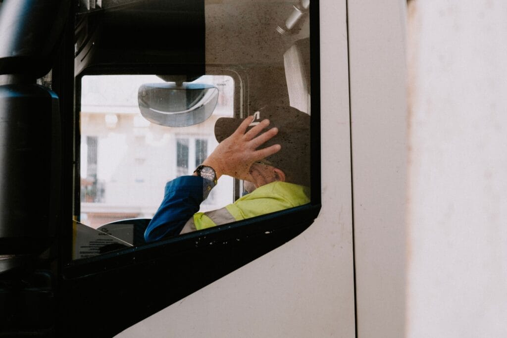 A truck driver in neon jacket rests with hand on head inside vehicle cabin, view from the side window. Operator fatigue was blamed as the primary cause of a crash on the SF Muni system in July 2026.