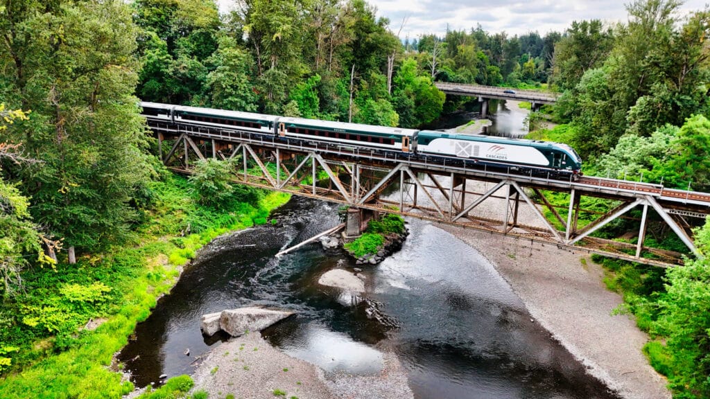 An Amtrak Airo train crosses over a bridge in the Pacific Northwest along the Cascades route in this promotional image from July 23, 2026. (Amtrak)